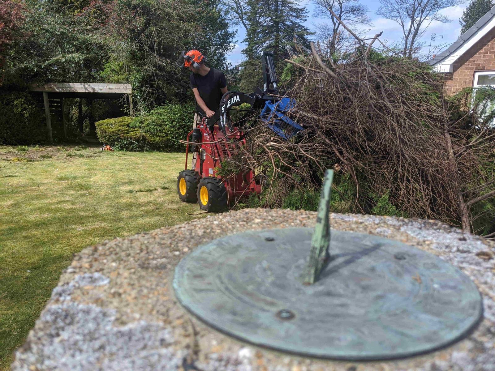 Operator in a helmet moving brush with a compact loader and grapple