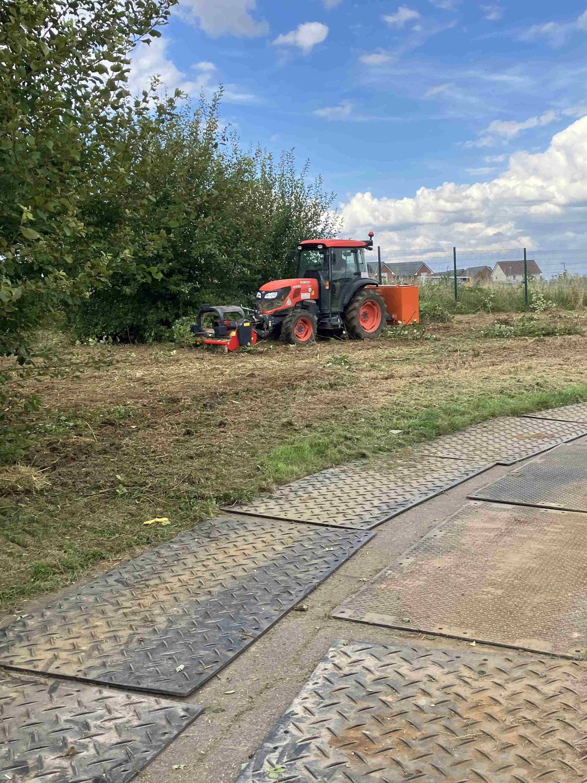 Compact tractor clearing scrub with ground protection mats laid out
